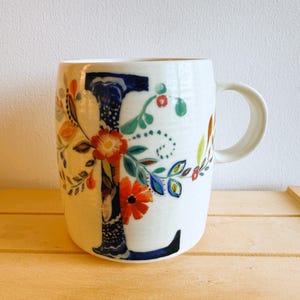 Vintage Petal Palette "L" mug designed by American fine artist, Starla M Halfmann. Halfmann designs for Anthropologie. Ridged, creamy-white mug. Fresh floral wrap-around design incorporates the letter "L".