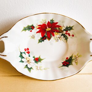 K&ouml;nnte beinhalten: Eine wei&szlig;e Porzellanservierschale mit goldener Verzierung und einem weihnachtlichen Blumendesign. Die Schale zeigt rote Weihnachtssterne, gr&uuml;ne Stechpalmenbl&auml;tter und wei&szlig;e Bl&uuml;ten.