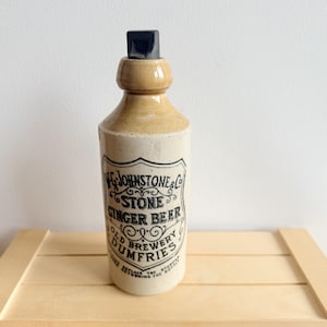 Peut inclure: Une bouteille de bière au gingembre en céramique de couleur crème avec un goulot vernissé beige et un bouchon noir. L'avant présente une étiquette imprimée en noir indiquant W. & J. JOHNSTONE & CO. STONE GINGER BEER OLD BREWERY DUMFRIES.