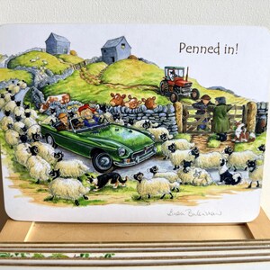 May include: A rectangular coaster featuring a colourful illustration of a green convertible car surrounded by a large flock of sheep on a country road. The scene includes a red tractor, stone walls, two small buildings, and the text Penned in!