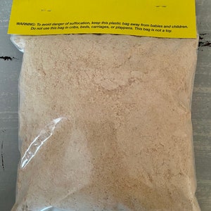 May include: A clear plastic bag filled with light brown material, sealed with a yellow header. The header has text warning about suffocation hazards and advises against use near children. The bag is on a gray surface.