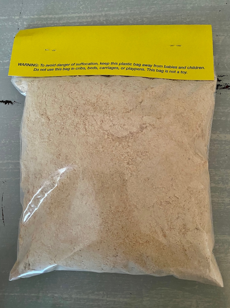 May include: A clear plastic bag filled with light brown material, sealed with a yellow header. The header has text warning about suffocation hazards and advises against use near children. The bag is on a gray surface.