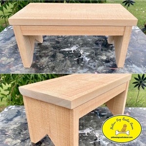 May include: A small, light-colored wooden step stool. The stool has a rectangular top and four angled legs. The wood grain is visible, giving it a rustic appearance. The stool is approximately 12 inches long, 8 inches wide, and 6 inches tall.