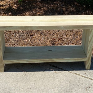 May include: A light-colored wooden bench with a lower shelf. The bench is made of unfinished wood and has a simple, rectangular design. The bench is approximately 48 inches long, 16 inches wide, and 18 inches high.