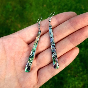 Puede incluir: Un par de pendientes colgantes de plata con detalles de abulón iridiscente verde, azul y morado.