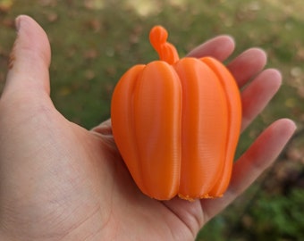 Puede incluir: Una pequeña calabaza naranja impresa en 3D con un tallo.
