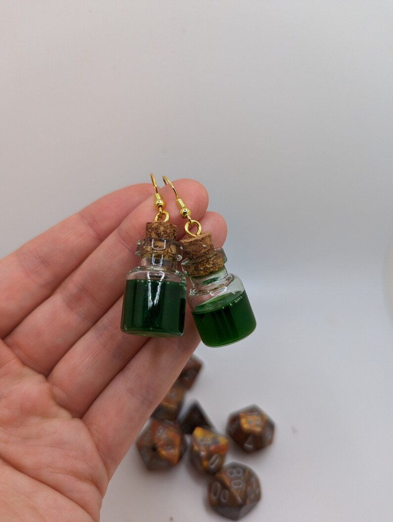 May include: A pair of gold earrings with small glass bottles filled with green liquid and cork stoppers.