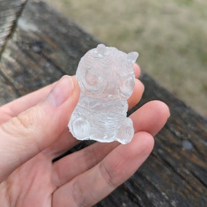 May include: A clear, translucent figurine of a small, cartoon-like creature with horns and large eyes. The figurine is made of a smooth, glassy material and has a detailed design.