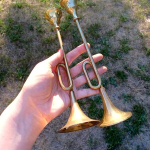 May include: Two gold trumpet-shaped candle holders with a flared bell-shaped base.