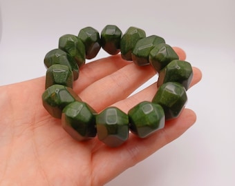 May include: A dark green faceted bead bracelet. The beads are a deep forest green color and have a geometric shape. The bracelet is displayed on a light background.