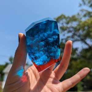May include: A blue and red resin geode with a faceted shape. The geode is filled with blue resin and white flecks, and the bottom is red.