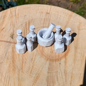 May include: A collection of small, light gray apothecary bottles and a mortar and pestle set on a wooden surface. The bottles are numbered from 1 to 7. The mortar and pestle also have the number 1 on them.
