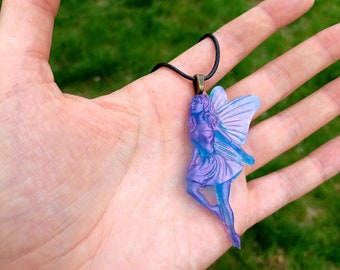 May include: A purple and blue iridescent fairy pendant necklace with a black cord. The fairy is depicted with wings and a flowing dress.