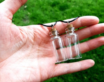 May include: Two small glass bottles with cork stoppers on black cords. The bottles are hanging from a hand.