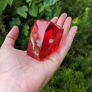May include: A large, bright red, faceted, glass paperweight. The paperweight is shaped like a diamond and has a smooth, polished surface.