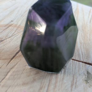May include: A faceted, dark purple crystal with a polished, reflective surface. The crystal has a geometric shape with multiple sides and angles, catching the light. The crystal is a decorative item, possibly for display or collection.