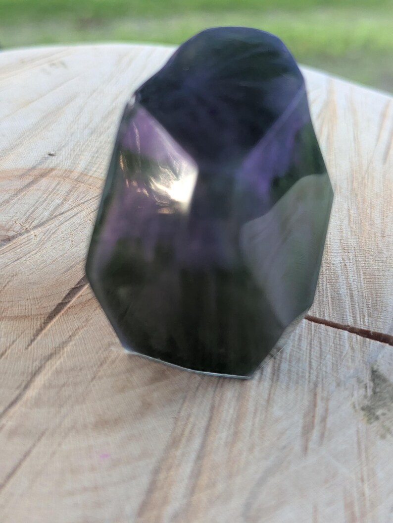 May include: A faceted, dark purple crystal with a polished, reflective surface. The crystal has a geometric shape with multiple sides and angles, catching the light. The crystal is a decorative item, possibly for display or collection.