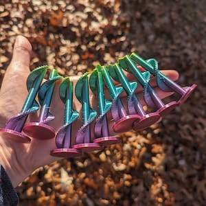 May include: A collection of 10 small, 3D printed, spiral-shaped objects. The objects are a gradient of green, blue, and purple colors. The bottom of each object is a flat, circular base that is a solid, dark purple color.