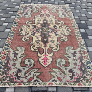 May include: A rectangular, vintage rug with a central medallion design. The rug has a reddish-brown field with beige, grey, and pink accents. The border is a mix of colours, including red, blue, and green, creating a traditional aesthetic.