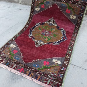 Puede incluir: Una alfombra roja, marr&oacute;n y verde con un patr&oacute;n y un borde con flecos. La alfombra tiene un dise&ntilde;o floral con un medall&oacute;n central.