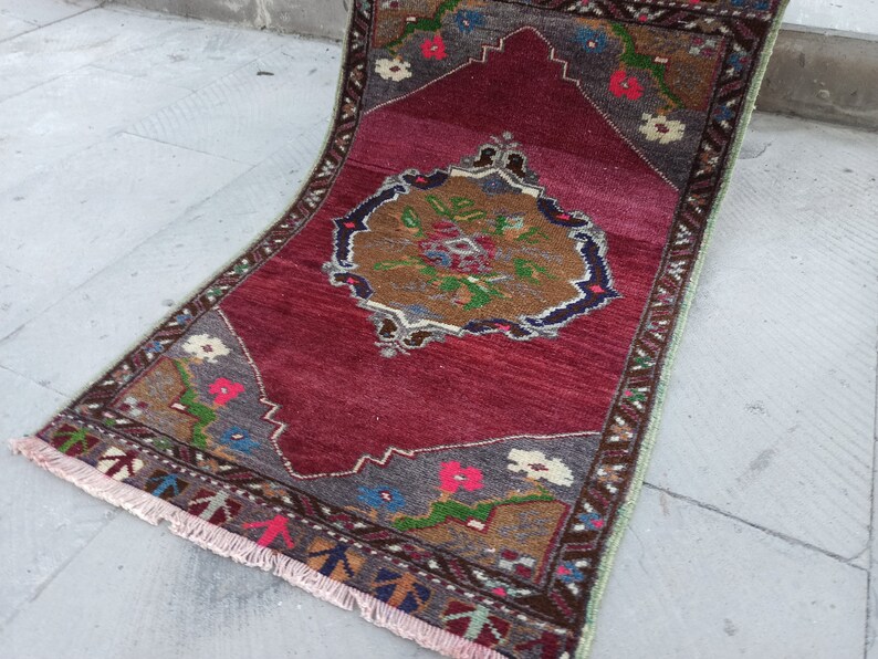 Puede incluir: Una alfombra roja, marr&oacute;n y verde con un patr&oacute;n y un borde con flecos. La alfombra tiene un dise&ntilde;o floral con un medall&oacute;n central.