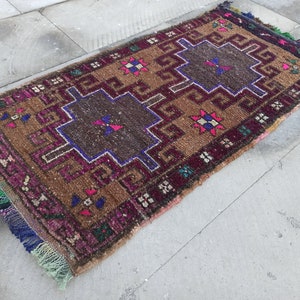 May include: A brown, pink and blue patterned rug with fringe on all sides. The rug has a geometric design with a central square.