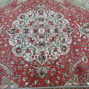 May include: A detailed shot of a red, green, and beige oriental rug. The rug features a central medallion design with floral and geometric patterns. The border is a darker red with intricate floral motifs. The rug's design is symmetrical and ornate.