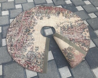 May include: Round, distressed rug with a floral pattern in shades of red, beige, and green. The rug has a circular cutout in the center and a section rolled back, revealing a similar design. The rug is placed on a gray and black tiled surface.