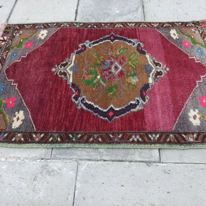 Puede incluir: Una alfombra roja, marr&oacute;n y verde con un dise&ntilde;o floral. La alfombra tiene un borde con flecos y est&aacute; hecha de lana.