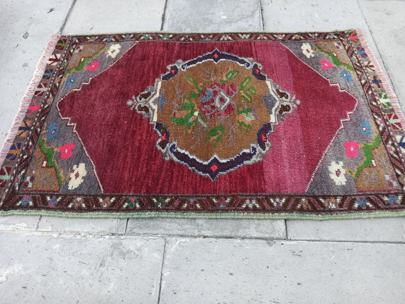 Puede incluir: Una alfombra roja, marr&oacute;n y verde con un dise&ntilde;o floral. La alfombra tiene un borde con flecos y est&aacute; hecha de lana.