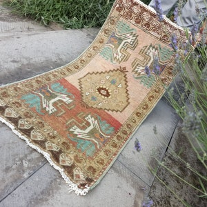 May include: A vintage Turkish rug with a geometric pattern in shades of brown, red, green, and blue. The rug has a fringe border and is folded in half.