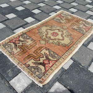 May include: A rectangular, hand-woven rug with a central medallion design. The rug features a warm color palette of orange, beige, and touches of red and brown. The edges have a fringed border. The rug's dimensions are approximately 60 x 122 cm.