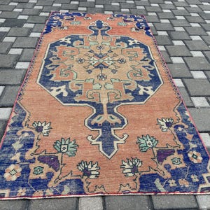 May include: A rectangular, vintage-style rug with a central medallion design. The rug features a warm peach-coloured field with intricate blue and teal floral patterns along the borders and within the central design. The rug is placed on a grey brick surface.