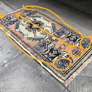 Puede incluir: Alfombra rectangular tejida a mano con un diseño tradicional. La alfombra presenta un campo central crema con intrincados patrones en negro, azul y melocotón. El borde es una mezcla de verde, melocotón y crema. Se ven flecos en los extremos.