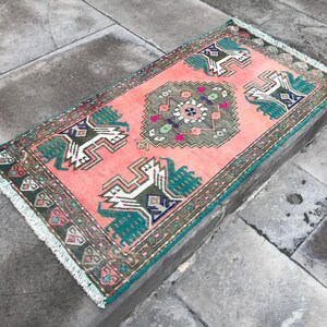 May include: A pink and green patterned rug with a fringed border. The rug features a traditional design with geometric shapes and floral motifs.