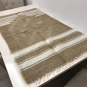 Puede incluir: Una alfombra de oración de rayas marrones y blancas con un borde de flecos. La alfombra está hecha de un material suave y peludo.