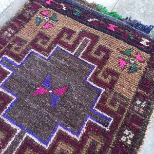 May include: A brown, red and blue patterned rug with a geometric design. The rug has a central square with a butterfly design.