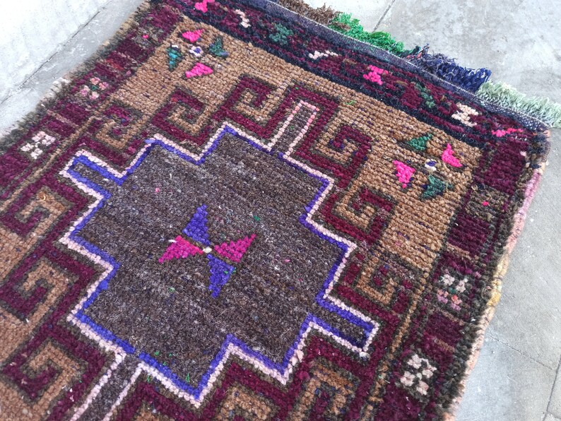 May include: A brown, red and blue patterned rug with a geometric design. The rug has a central square with a butterfly design.