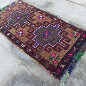 May include: A brown, red and blue patterned rug with fringe. The rug has a geometric design with a central square.