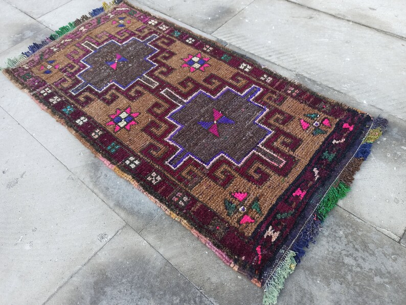 May include: A brown, red and blue patterned rug with fringe. The rug has a geometric design with a central square.