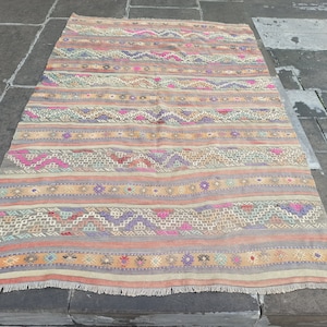 May include: A vintage Turkish kilim rug with a colorful striped pattern featuring geometric designs in shades of pink, purple, blue, and beige.