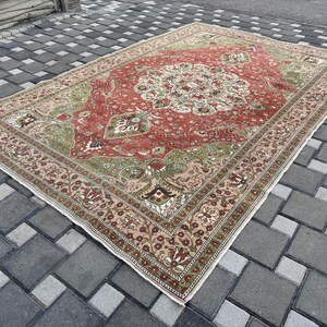 May include: A rectangular, vintage-style rug with a central medallion design. The rug features a red field with green and cream accents, and a detailed border in shades of pink and brown. The rug is placed on a gray brick surface.
