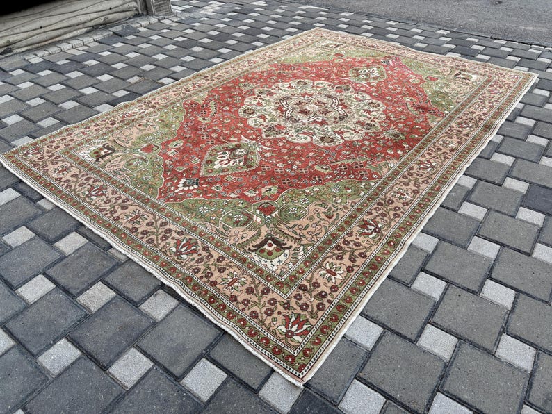 May include: A rectangular, vintage-style rug with a central medallion design. The rug features a red field with green and cream accents, and a detailed border in shades of pink and brown. The rug is placed on a gray brick surface.