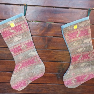 May include: Two red, brown, and beige patterned Christmas stockings with blue trim. The stockings are hanging from a wooden surface.