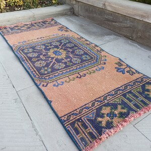 May include: A long, narrow rug with a pink background and a blue, green, and brown geometric pattern. The rug has a fringe border.