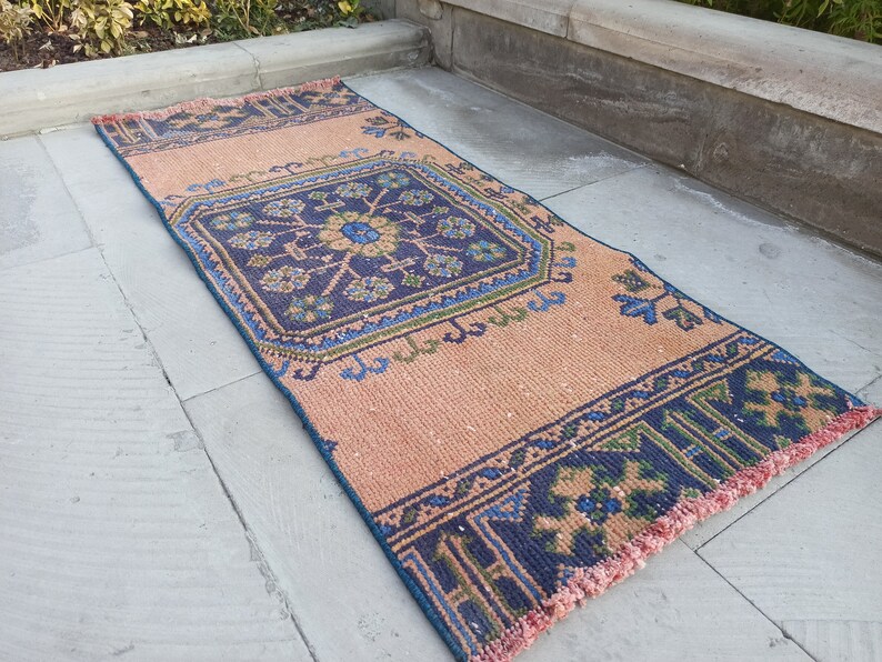 May include: A long, narrow rug with a pink background and a blue, green, and brown geometric pattern. The rug has a fringe border.