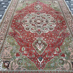 May include: A rectangular, vintage-style rug with an intricate, floral-inspired design. The rug features a central red field with a detailed medallion and corner accents in green, beige, and cream. The border is a mix of beige and red, creating a classic, ornate look.