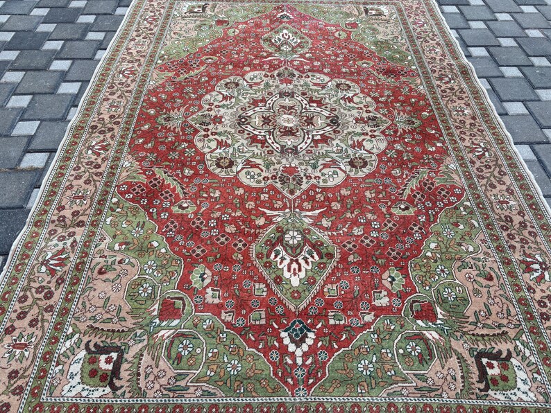 May include: A rectangular, vintage-style rug with an intricate, floral-inspired design. The rug features a central red field with a detailed medallion and corner accents in green, beige, and cream. The border is a mix of beige and red, creating a classic, ornate look.
