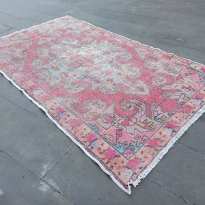 May include: A pink and white vintage rug with a floral pattern. The rug has a fringed edge and is made of wool.