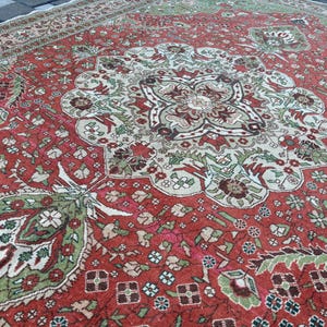 May include: A detailed, antique rug with a central medallion design. The rug features a rich red background with intricate patterns in shades of green, brown, and cream. The border has a complementary design, creating a cohesive and ornate look.